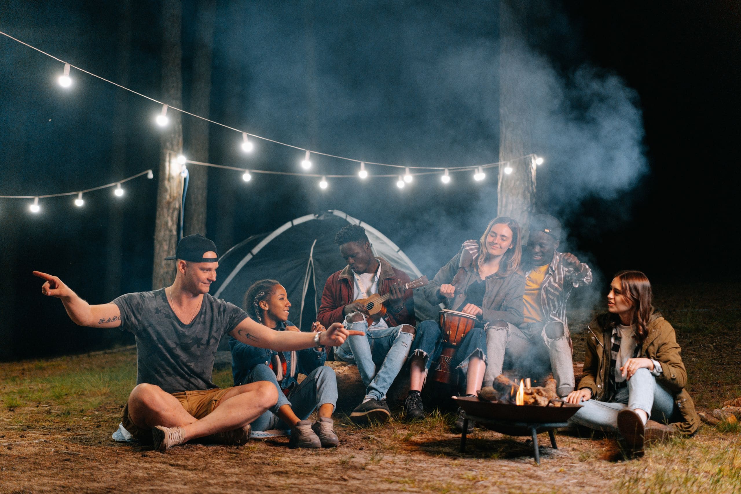 Friends gathered around a glamping fire pit between canvas tents under a starlit sky
